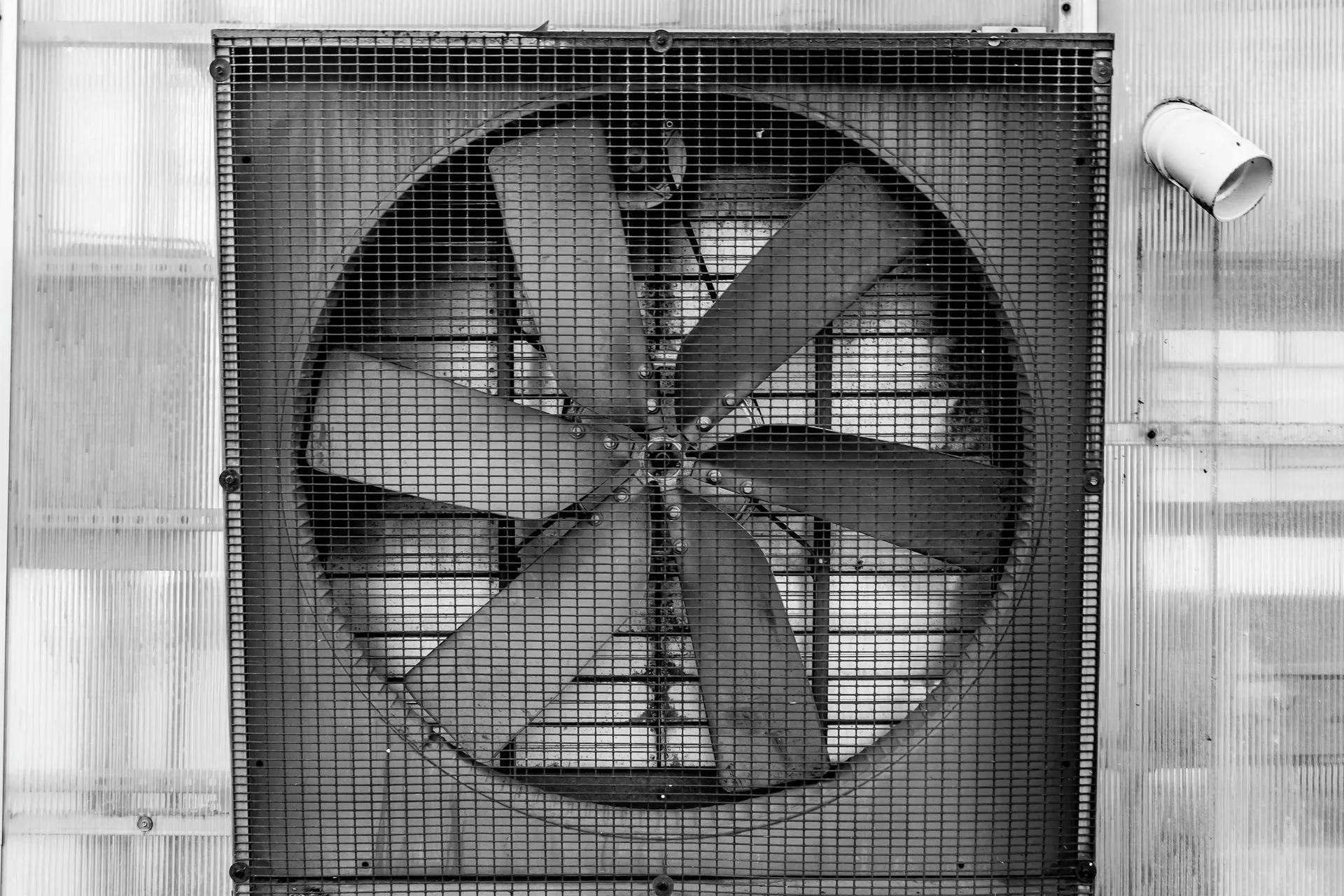 A black and white photo of a large fan on the side of a building.